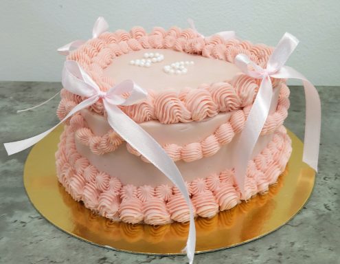 Pastel de bodas de dos niveles decorado en rosa con lazos blancos y flores de crema.